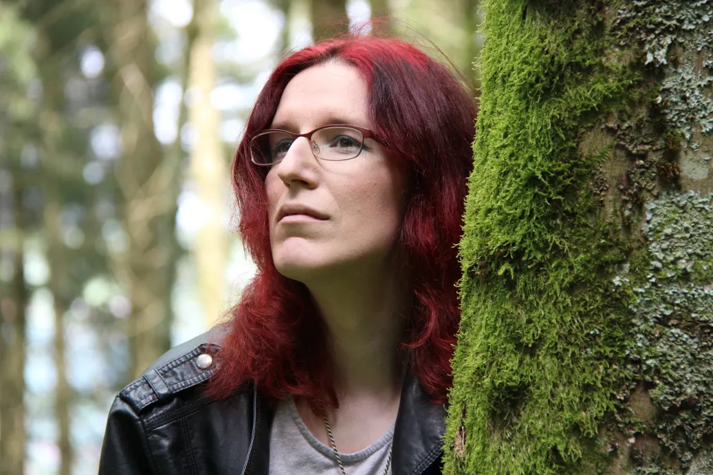 Viktoria Rei Bauer im Wald, neben einem moosbewachsenen Baum